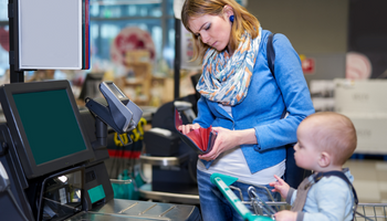 Woman standing at checkout with baby in cart looking through wallet