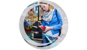 Woman standing at checkout with baby in cart looking through wallet